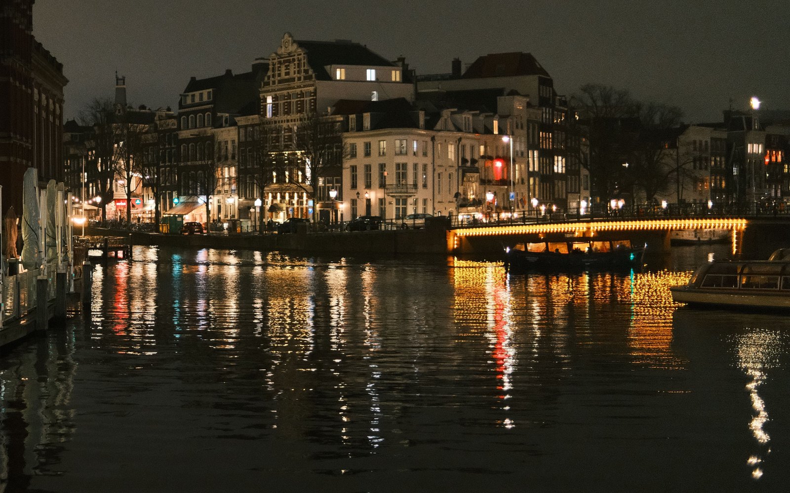 Canal de Ámsterdam de noche, con un puente iluminado y las casas reflejadas en el agua