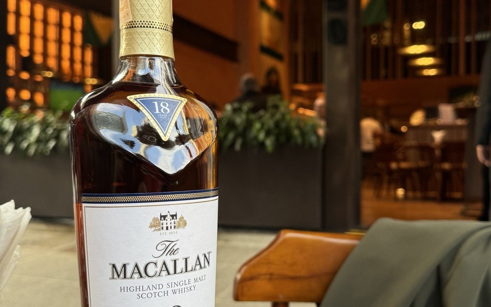 Garrafa de The Macallan 18 anos Double Cask numa mesa de madeira, com a fachada de um restaurante ao fundo