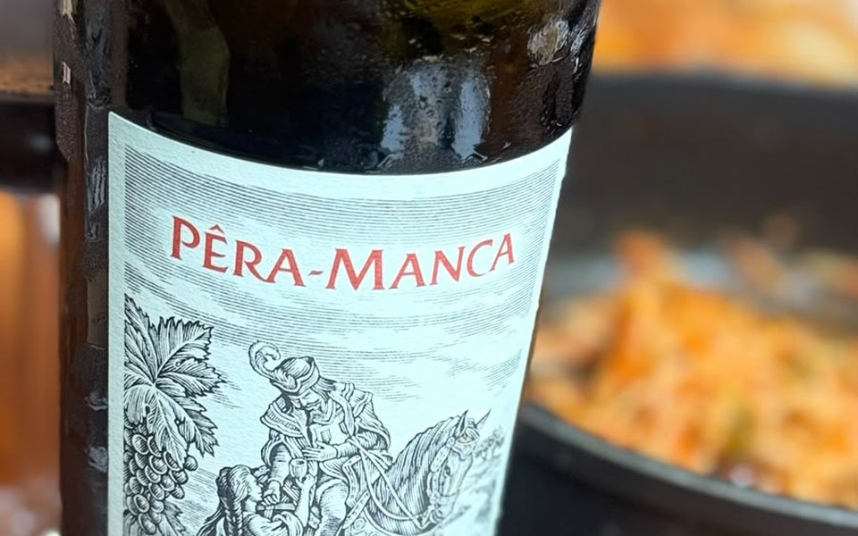 Rótulo do Pêra-Manca tinto 2011, com a gravura do cavaleiro e do cacho de uvas, e um tacho ao fundo