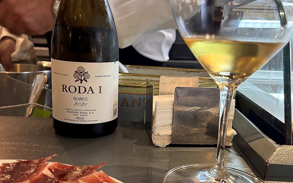 Garrafa de Roda I Blanco 2021 e uma taça de vinho branco num balcão